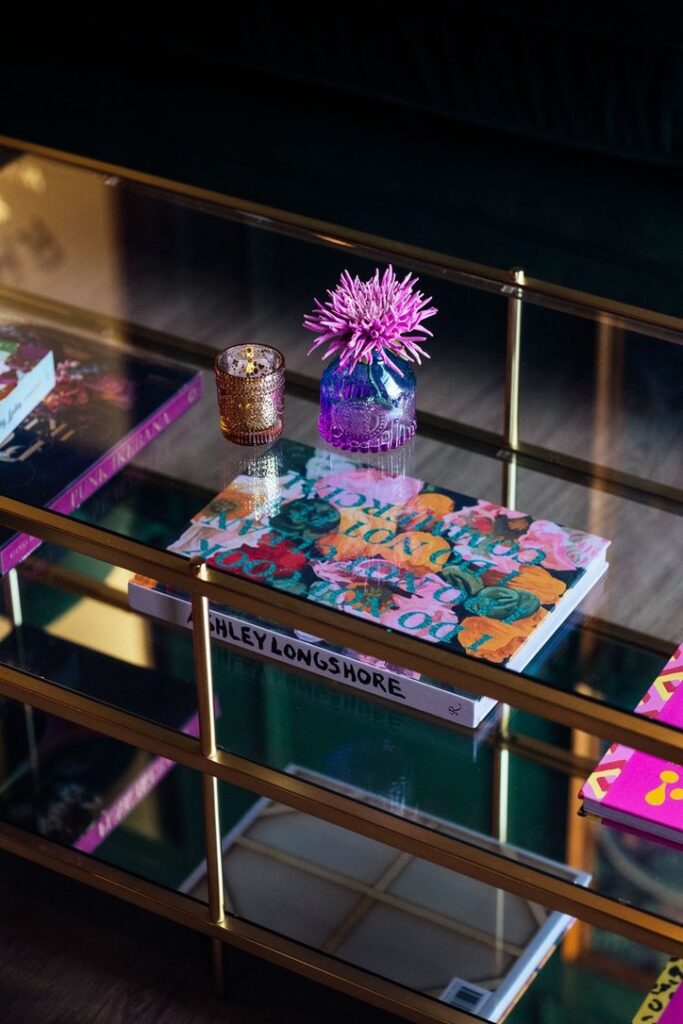 Detail of a glass coffee table with stacked books, a candle, and floral arrangement.