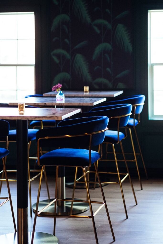 Detail view of restaurant seating with marble tables and blue velvet chairs.