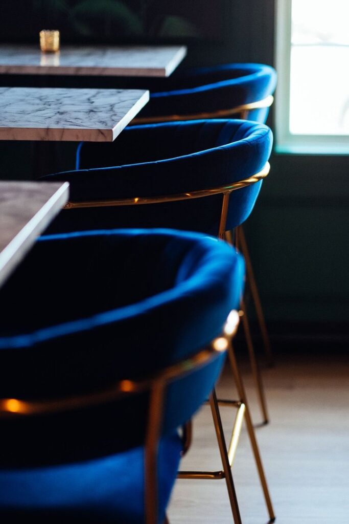 Up-close view of restaurant seating with marble tables and blue velvet chairs.
