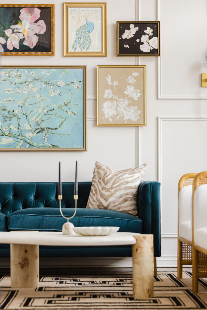 A styled living room featuring a teal velvet sofa, a gold-framed gallery wall, and a sculptural stone coffee table.