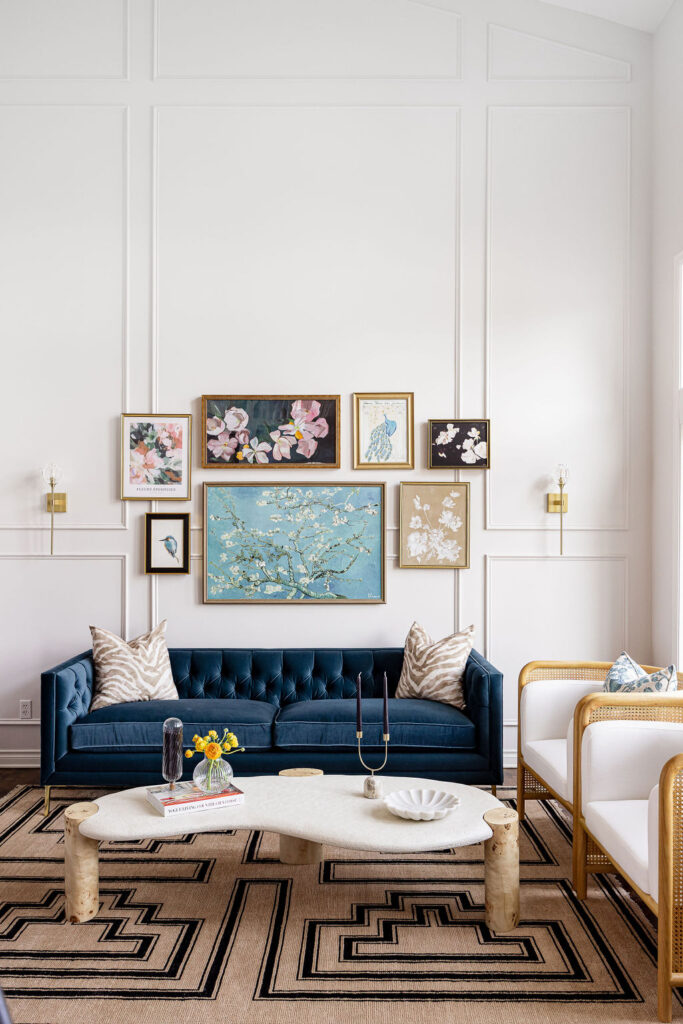 A beautiful photo showing a stunning custom-created interior design project in Plymouth. At the bottom of the page, a blue couch with two zebra print pillows. A collection of art in various frames and sizes is centered above the sofa. The wall is white and has beautiful white picture frame molding. The design and furniture work great together and is balanced.