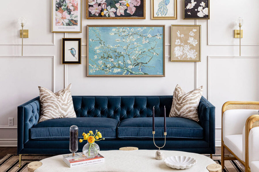 A beautiful photo showing a stunning custom-created interior design project in Plymouth. At the bottom of the page, a blue couch with two zebra print pillows. A collection of art in various frames and sizes is centered above the sofa. The wall is white and has beautiful white picture frame molding. The design and furniture work great together and is balanced.