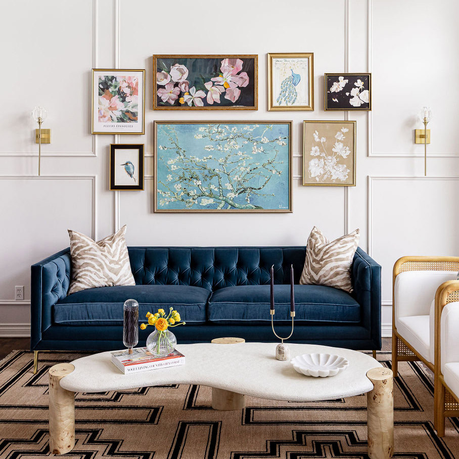 A beautiful photo showing a stunning custom-created interior design project in Plymouth. At the bottom of the page, a blue couch with two zebra print pillows. A collection of art in various frames and sizes is centered above the sofa. The wall is white and has beautiful white picture frame molding. The design and furniture work great together and is balanced.