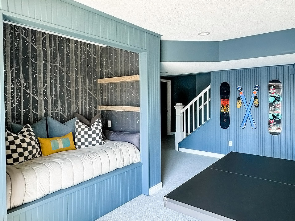 Lower level with blue walls, skis and snowboards hanging on the wall, and a cozy reading nook that's built into the wall. Wonderful interior design by the Firelight Style House.