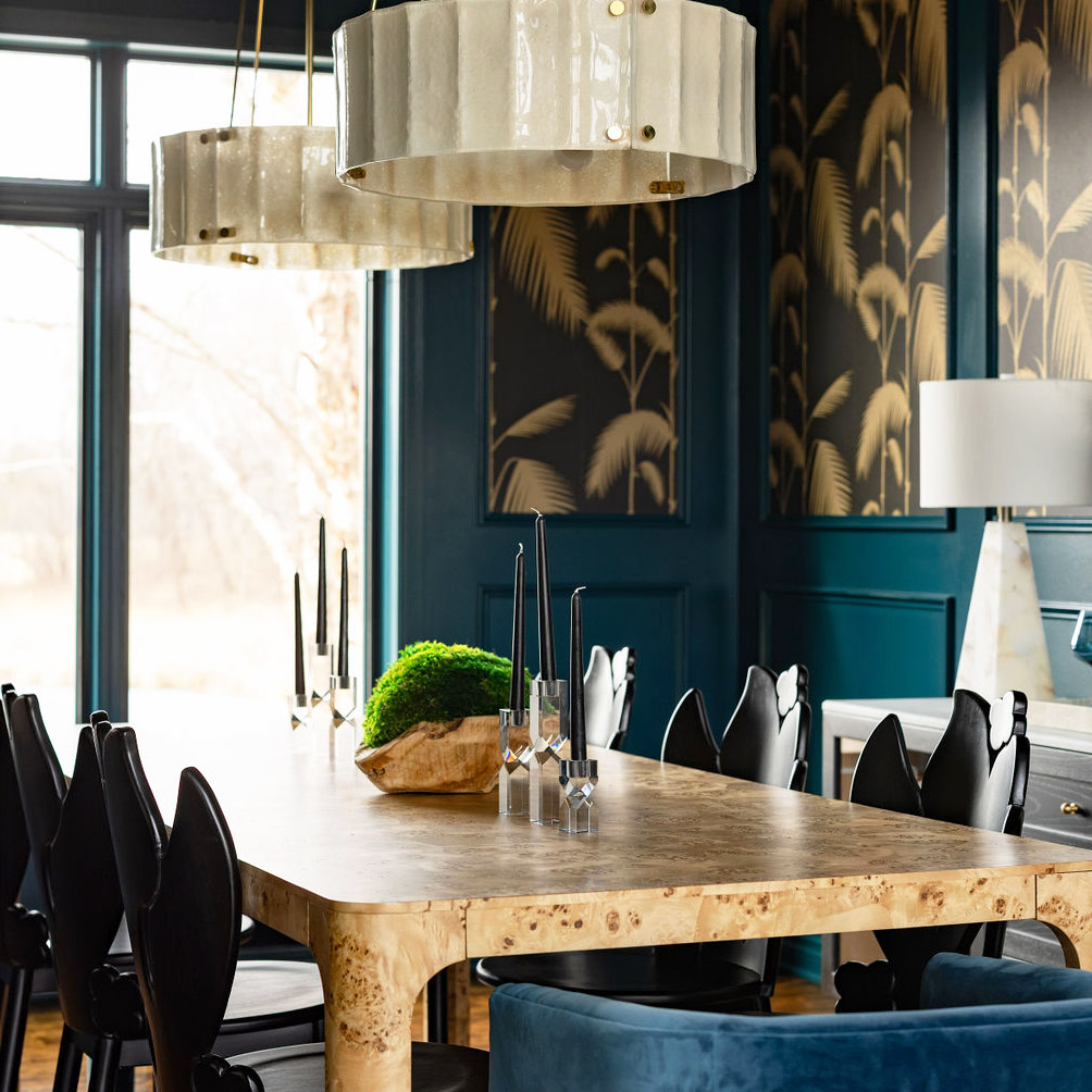 A picture of the newly finished redesigned interior of a dining room. Dark green walls, framed modeling with wallpaper in it that's black with cream colored plant leaves. There are contemporary tables and chairs.