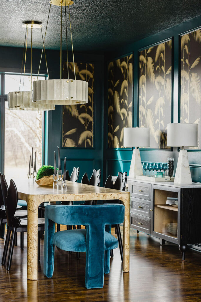 A picture of the newly finished redesigned interior of a dining room. Dark green walls, framed modeling with wallpaper in it that's black with cream colored plant leaves. There are contemporary tables and chairs.