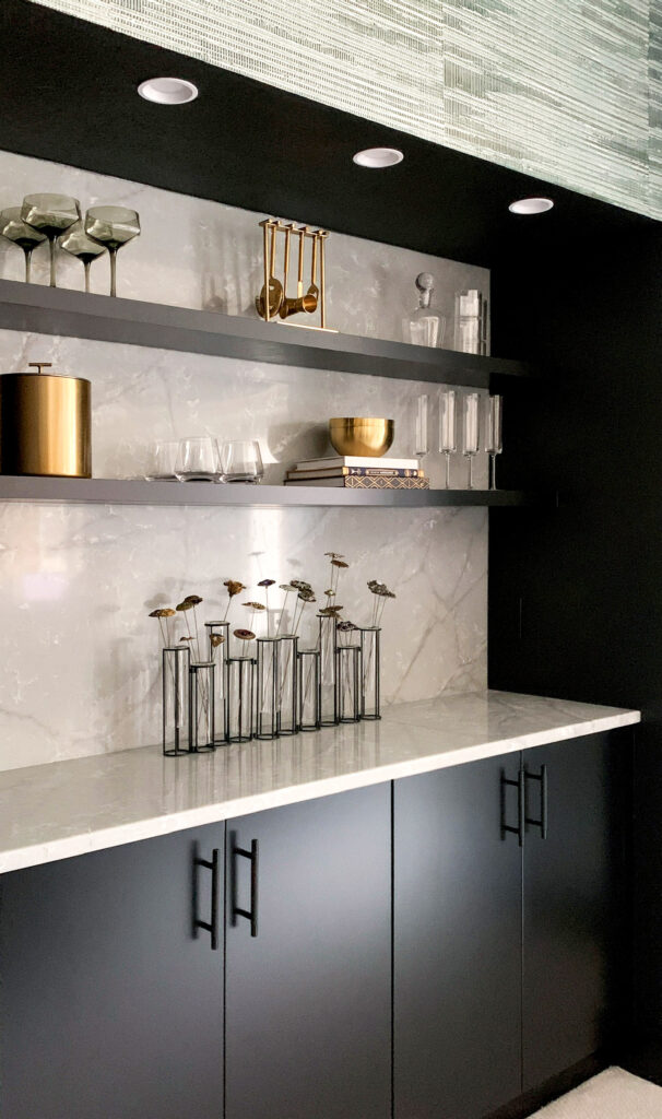 Custom remodeled bar with black cabinets, marble backsplash, and styled shelving in modern interior.