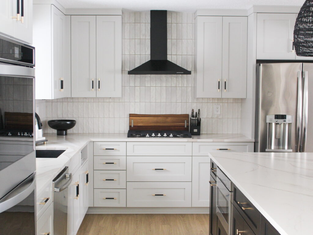 Contemporary kitchen in the Minneapolis suburbs with a black vent hood, stainless steel appliances, and clean tile backsplash set against warm wood floors.