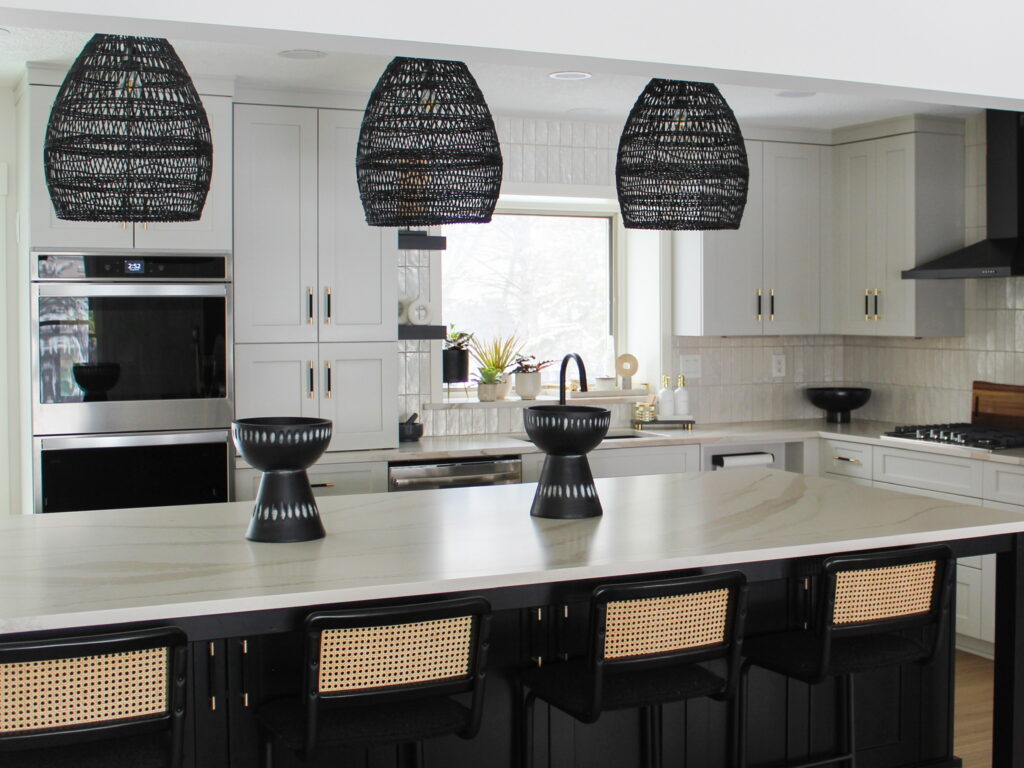 A spacious kitchen remodel near Minneapolis features black rattan lighting, a matte black island with seating, and a bright tile backsplash paired with custom white cabinetry. This design showcases the Firelight team's boutique creativity and expertise in blending bold contrasts with clean elegance.