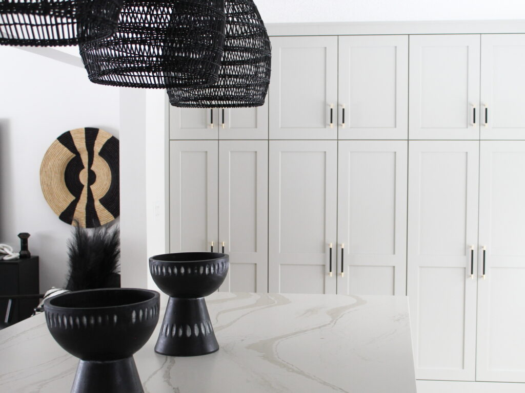 A close-up of a fully remodeled Minneapolis-St. The Paul Modern Hacienda kitchen, designed by the Firelight Style House design team, features light cabinetry with matte black hardware and decorative woven art on the wall.