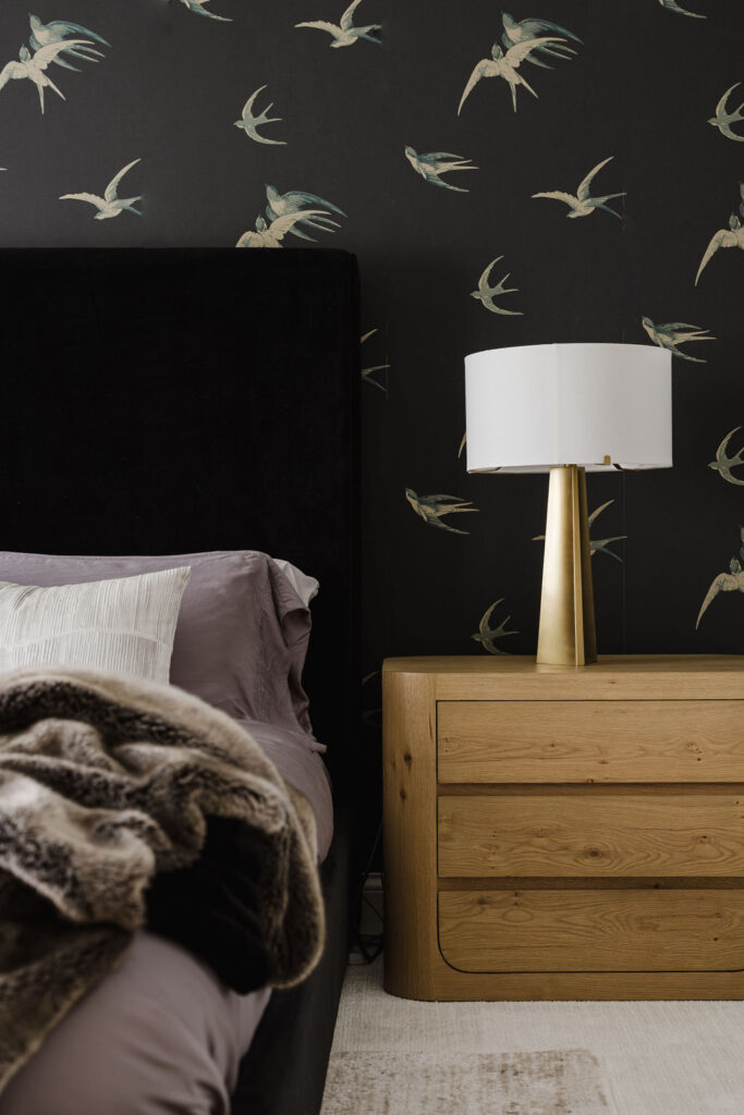 Minneapolis-St. Paul bedroom remodel with bird-print wallpaper, oak nightstand, brass lamp, and black velvet bed with lavender bedding.