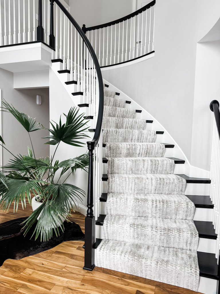 Curved staircase in a Minneapolis-St. Paul's home has white spindles, dark railing, and a patterned carpet runner over hardwood flooring.