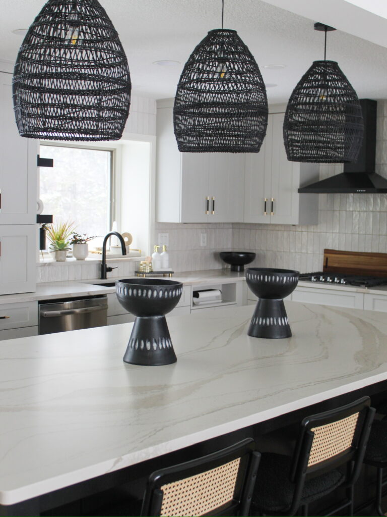 This bright modern kitchen in the Minneapolis-St. Paul area features woven black pendant lights above a sleek marble island, with black-and-natural woven bar stools and matte black fixtures creating contrast.