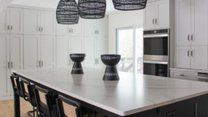 This bright modern kitchen in the Minneapolis-St. Paul area features woven black pendant lights above a sleek marble island, with black-and-natural woven bar stools and matte black fixtures creating contrast.