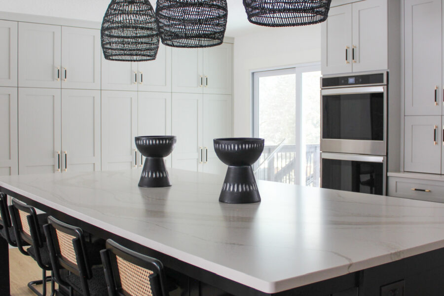 This bright modern kitchen in the Minneapolis-St. Paul area features woven black pendant lights above a sleek marble island, with black-and-natural woven bar stools and matte black fixtures creating contrast.