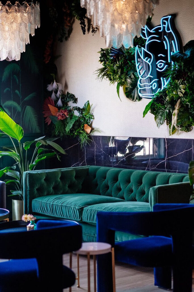 A closer angle of the lounge at Rhino Wine Bar, highlighting the dramatic mix of jungle-inspired décor and a glowing neon rhino sign. The green velvet sofa, crystal lighting, and abundance of plant life reflect the interior design team's imaginative, boutique approach to hospitality design in the Minneapolis-St. Paul area.