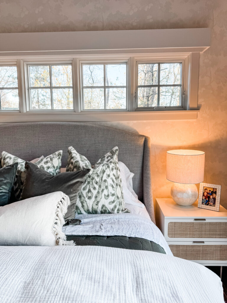 up close of a beautifully made bed with a grey headboard and night stand details.
