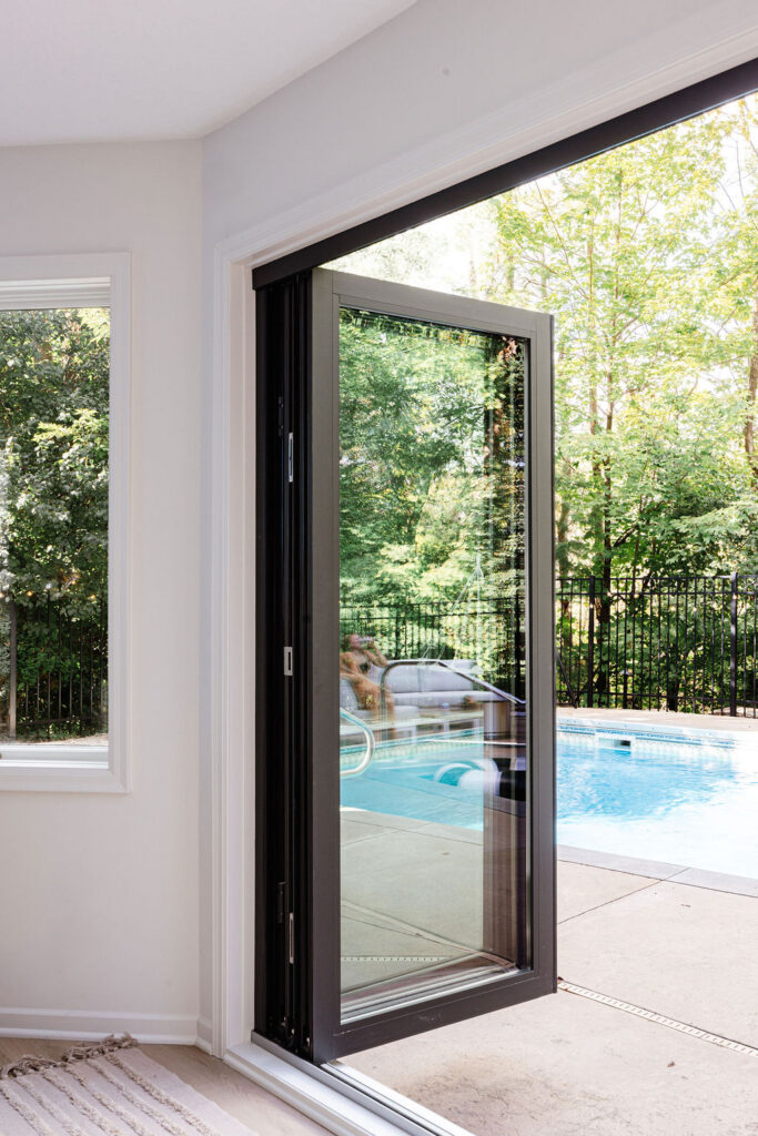 Modern black-framed sliding glass door opening to an outdoor pool and patio, with trees visible beyond the fence.