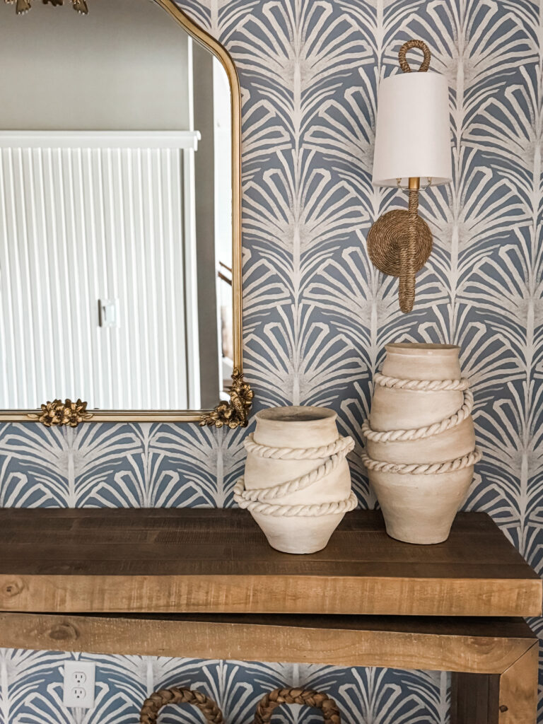 Up close of blue wallpaper with a mirror, sconce and console table.