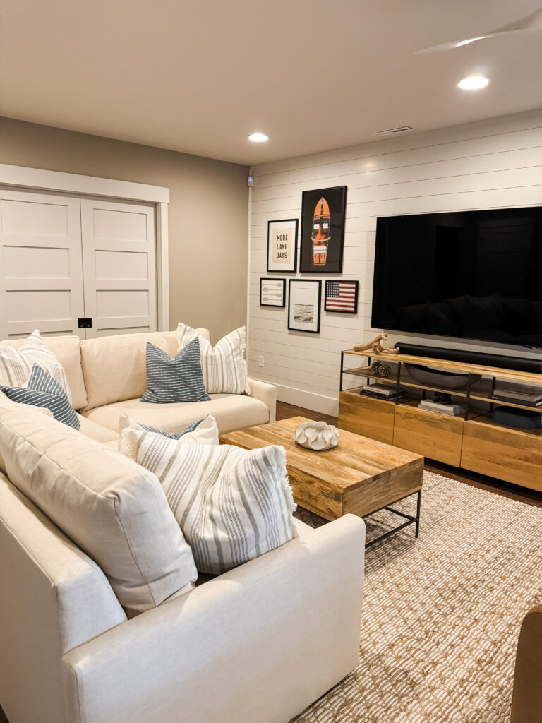 A white sectional with blue throw pillows in front of a wooden coffee table and tv console.