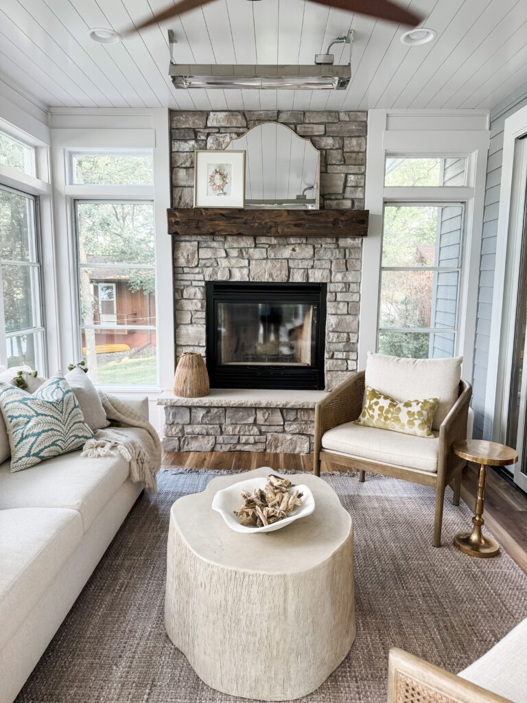 A sunroom with a cream couch, a palm throw pillow, a rattan accent chairs and a cream coffee table.
