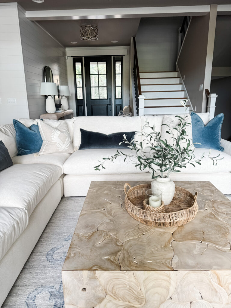A cream sectional with different hues of blue accent pillows with a wooden coffee table with decor.