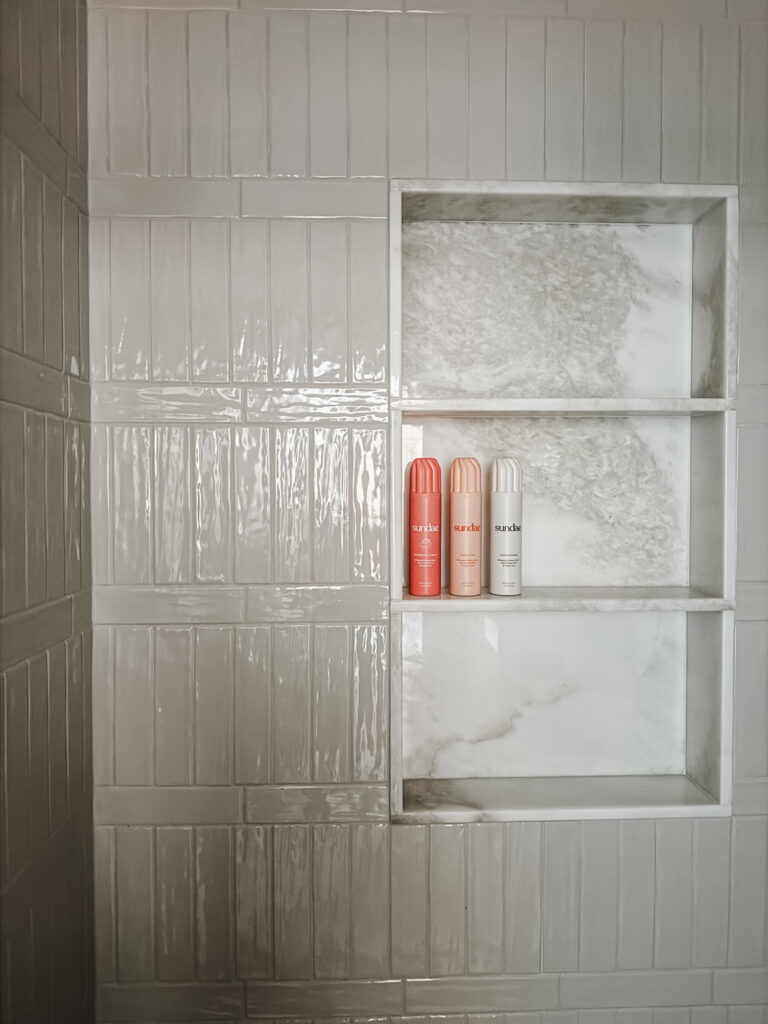 cream subway tile with marble shower niche with three bright bottles of soap