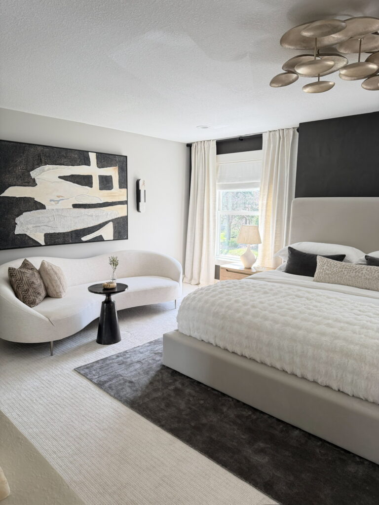 Modern neutral bedroom design with upholstered bed, curved sofa, abstract artwork, and statement brass chandelier