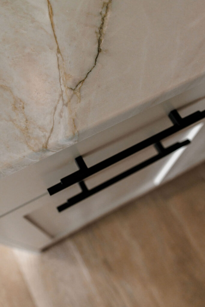 up close view of a kitchen cabinet corner showcasing black metal cabinet pulls and veining on the counterop
